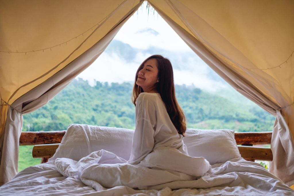 A young woman waking up in the morning with a beautiful nature view outside the tent